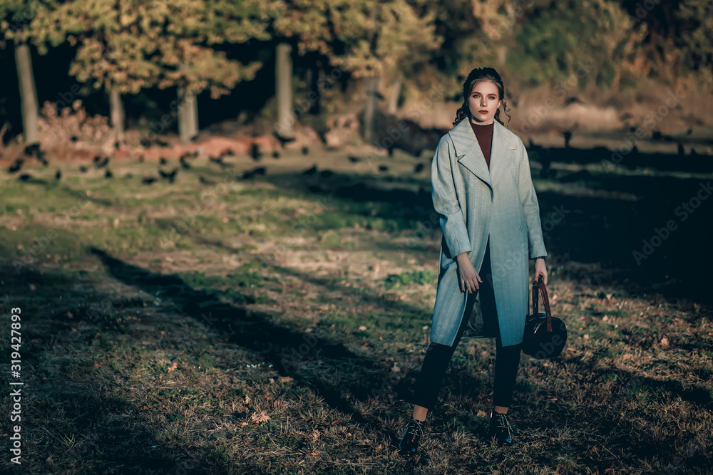 Young fashionable beautiful girl in a long gray coat, black jeans and with a dark red bag. Portrait shooting of a stylish girl. Facial shooting, street style and fashion. Professional model. Young fashionable beautiful girl in a long gray coat, black jeans and with a dark red bag. Portrait shooting of a stylish girl. Facial shooting, street style and fashion. Professional model.