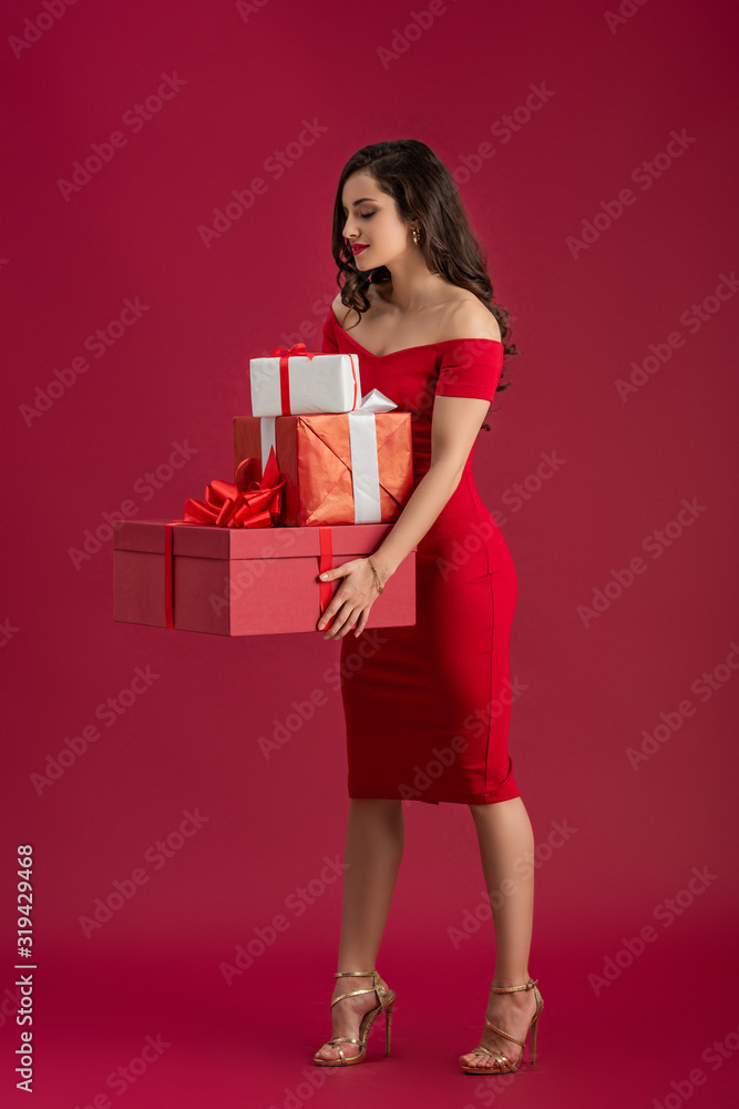 sexy, elegant girl holding gift boxes and smiling while standing on red background sexy, elegant girl holding gift boxes and smiling while standing on red background