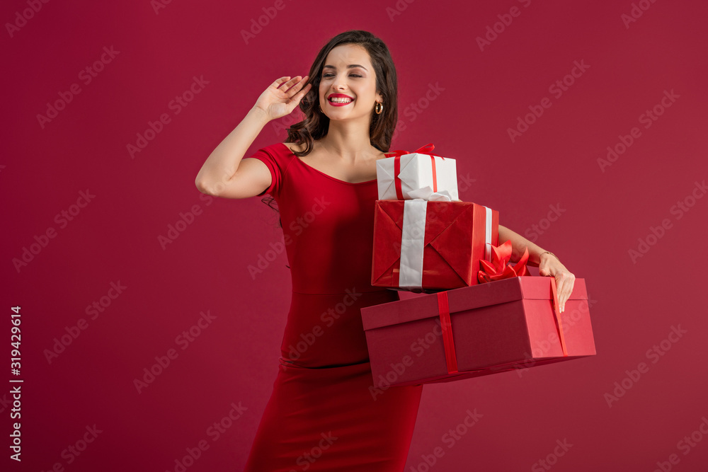 sexy, happy girl looking away and waving hand while holding gift boxes isolated on red sexy, happy girl looking away and waving hand while holding gift boxes isolated on red