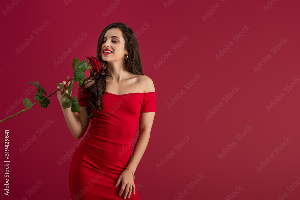 seductive, elegant girl enjoying flavor of red rose with closed eyes isolated on red seductive, elegant girl enjoying flavor of red rose with closed eyes isolated on red