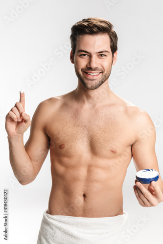 Photo of joyful half-naked man smiling and showing facial cream