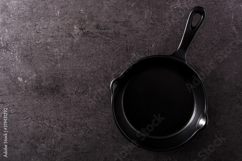 Iron frying pan empty on black slate background. Top view. Copy space