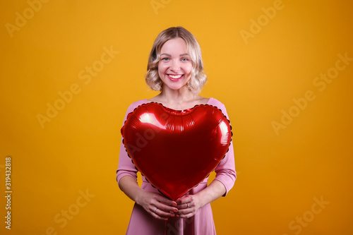 Portrait of young blonde woman posing with helium inflated air balloon. Happy valentine's day concept. Happy female with curled hair over colorful background. Close up, copy space for text. © Evrymmnt
