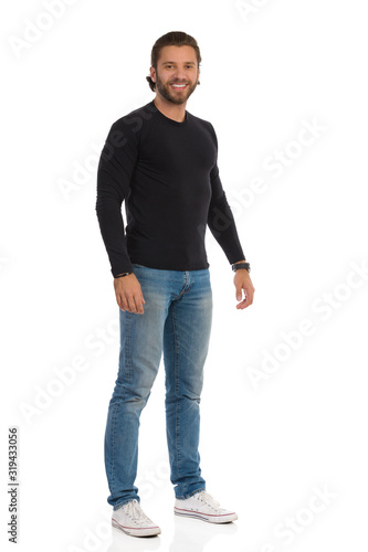 Relaxed Man In Black Jersey, Jeans And Sneakers Is Standing And Looking At Camera.