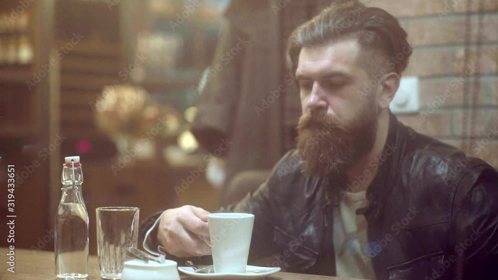 Bearded man in cafe. Serious man drinking a cup of coffee in the cafe. Confident successful man relaxing in outdoors cafe looking pensive. Man drinking expresso coffee Bearded man in cafe. Serious man drinking a cup of coffee in the cafe. Confident successful man relaxing in outdoors cafe looking pensive. Man drinking expresso coffee