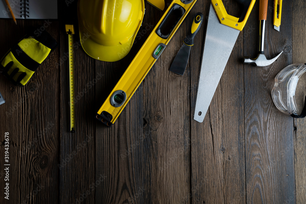 Contractor concept. Tool kit of the contractor: yellow hardhat, libella, hand saw, and notebook on the rustic wooden background.