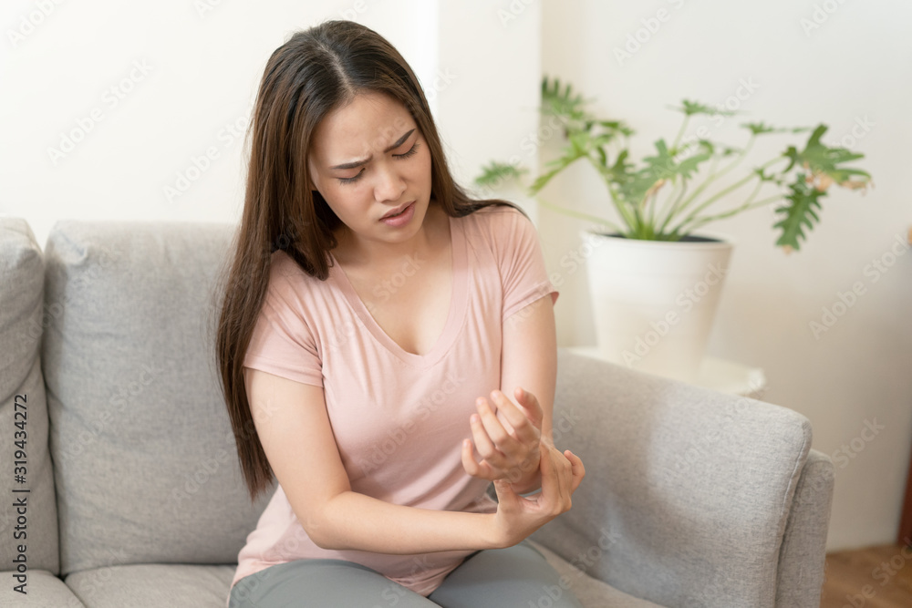 Asian girl having Wrist Pain sitting on sofa at home. young girl has pain arthritis, Health and illness concepts Asian girl having Wrist Pain sitting on sofa at home. young girl has pain arthritis, Health and illness concepts