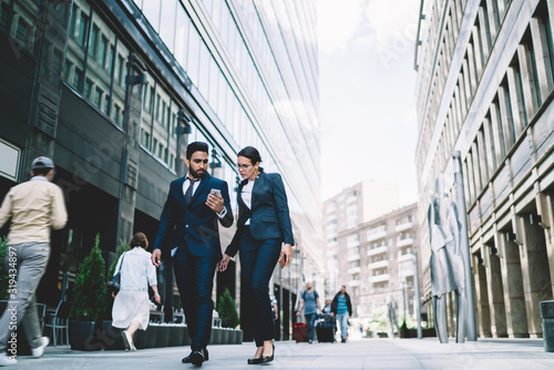 Foto Serious business partner walking in downtown street with browsing smartphone on