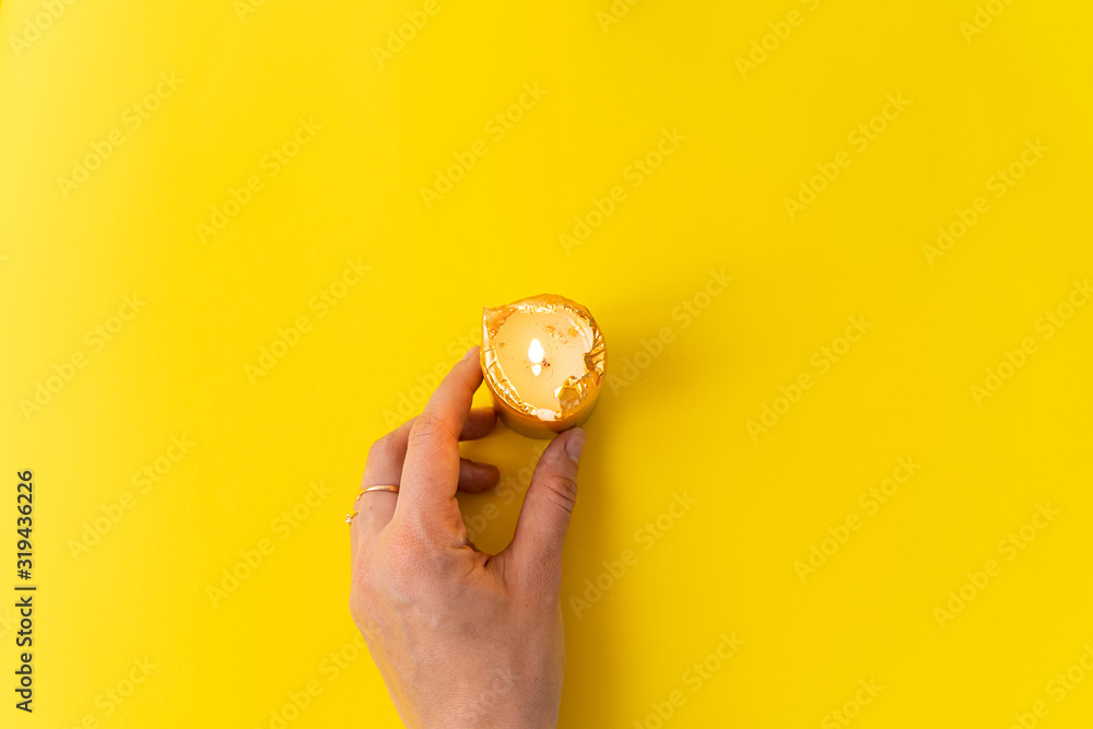 Hand with golden candles on yellow background. Wellnes, magic, relax concept. Copy space - obrazy, fototapety, plakaty 