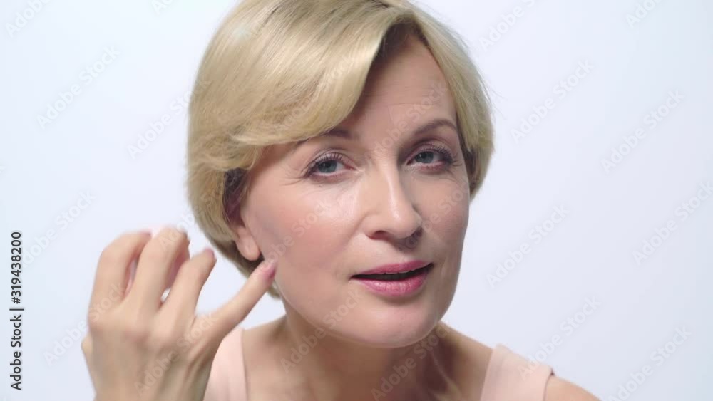 mature woman holding makeup puff near face isolated on white mature woman holding makeup puff near face isolated on white
