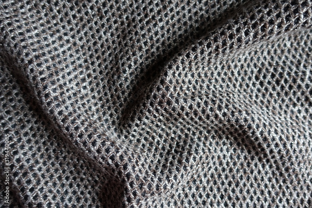 Thick greyish brown woolen fabric with diamond pattern in soft folds Thick greyish brown woolen fabric with diamond pattern in soft folds