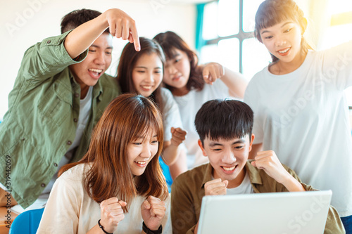 excited college students looking at laptop  in classroom