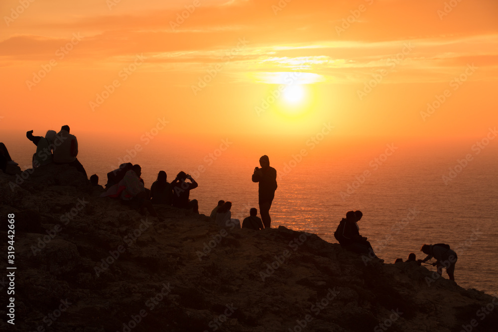 Silhouette of people sitting on a rock watching the sunset in front of the sea