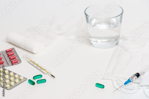 Laboratory table with a respiratory mask, pills, syringe, glass with water, thermometer. White background. 2019 nKoV Coronavirus originating in Wuhan, China.