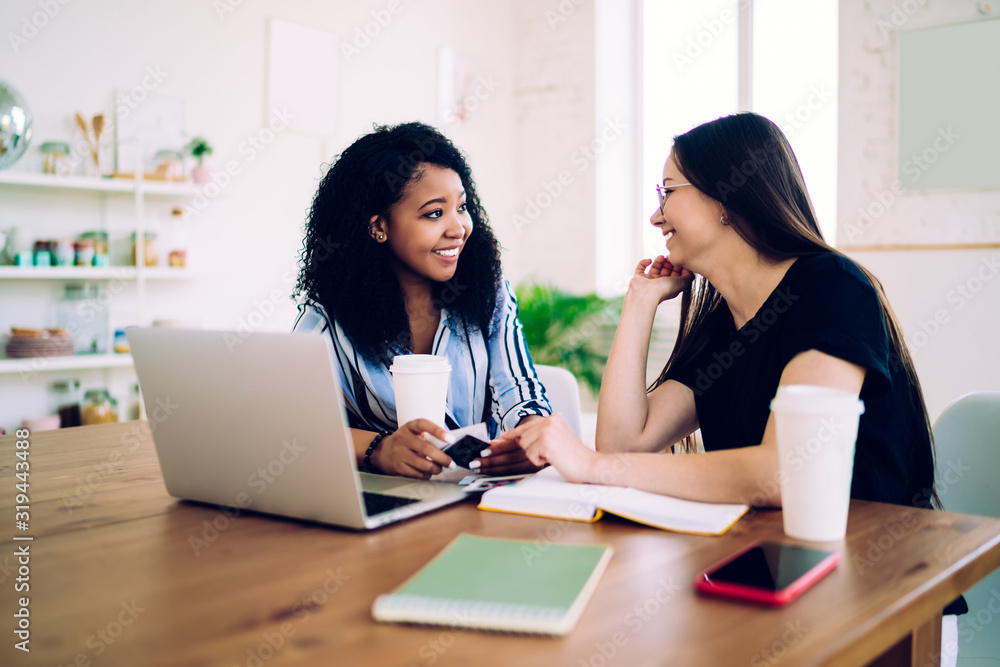 Multiracial women sincerely talking at table with laptop Multiracial women sincerely talking at table with laptop