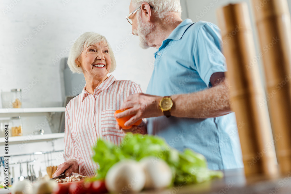Selective focus of smiling woman looking at husband while cooking on kitchen table Selective focus of smiling woman looking at husband while cooking on kitchen table