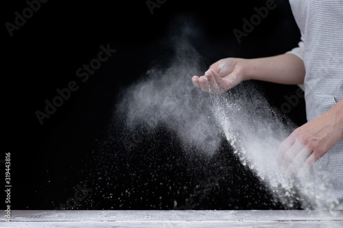 Professional cook in a kitchen sprinkles flour on the table to make dough. Empty space for text. Isolated on dark background