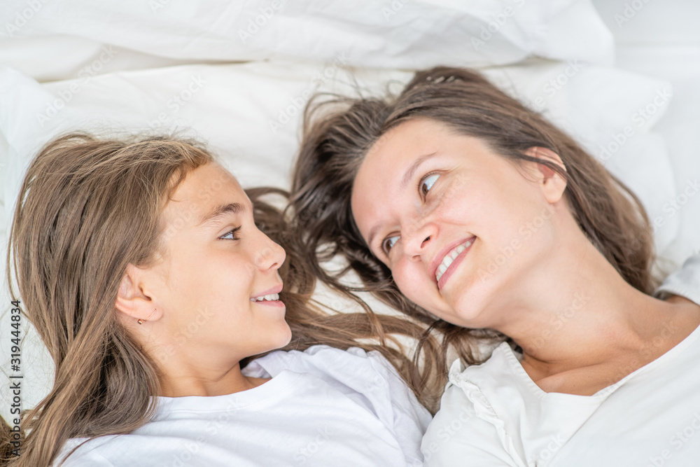 Young woman lies with her little daughter on the bed before bedtime. Happy family concept