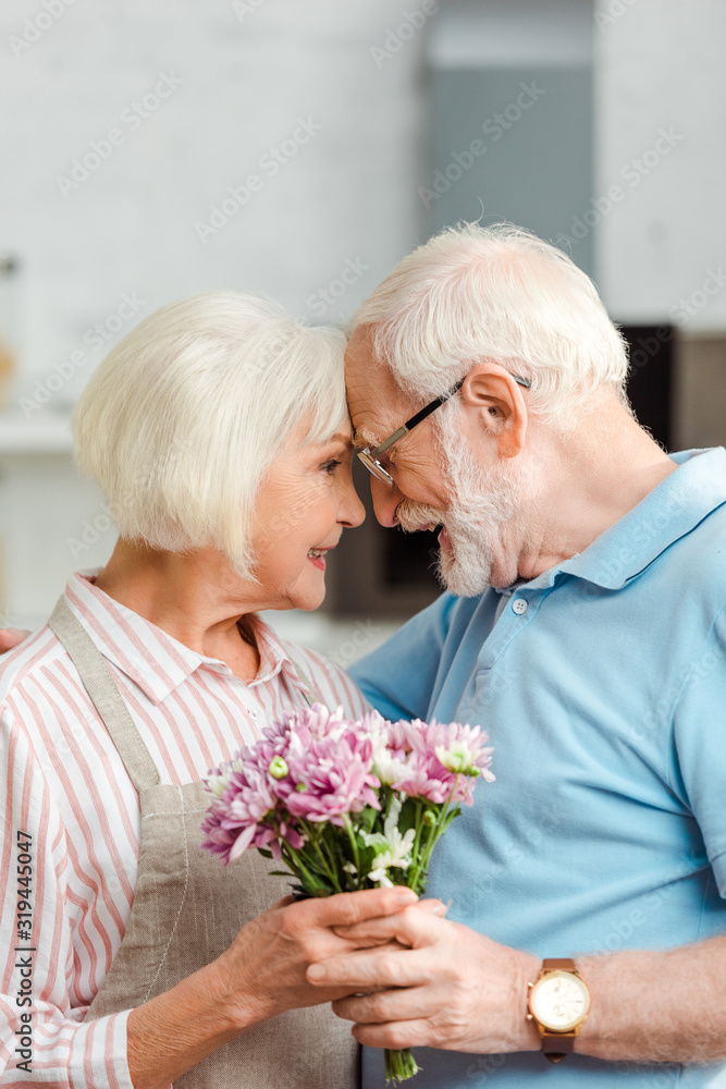 Side view of senior couple holding bouquet and smiling at each other at home Side view of senior couple holding bouquet and smiling at each other at home