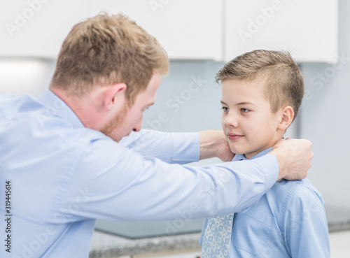 Dad helps son tie a tie at home