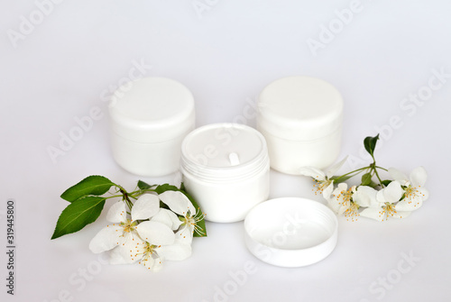 Cosmetics for hand and face care in white jars on a light background and spring flowers of a blossoming apple tree. Still life in high key. Place for text  soft light  close-up