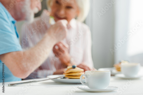 Selective focus of senior couple smiling at each other by coffee and pancakes on table