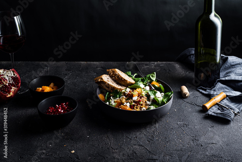 Buckwheat salad with lamb's lettuce, pomegranat seeds, goat cheese, mandarine and spring onion, Served with whole grain baguette and red wine. Black table and black background.