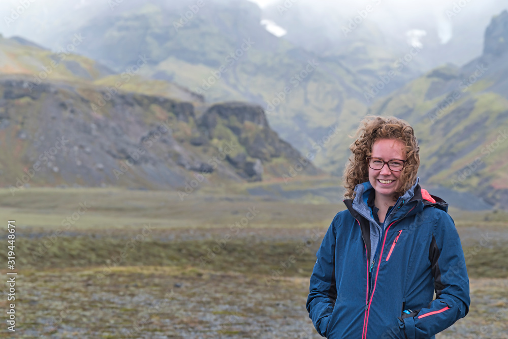 One woman is smiling at camera, wind blows through her hair, the highlands and the glacier and the moss covered mountains in background, Iceland
