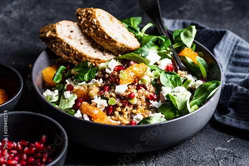 Fotografia Buckwheat salad with lamb's lettuce, pomegranat seeds, goat cheese, mandarine and spring onion, Served with whole grain baguette and red wine
