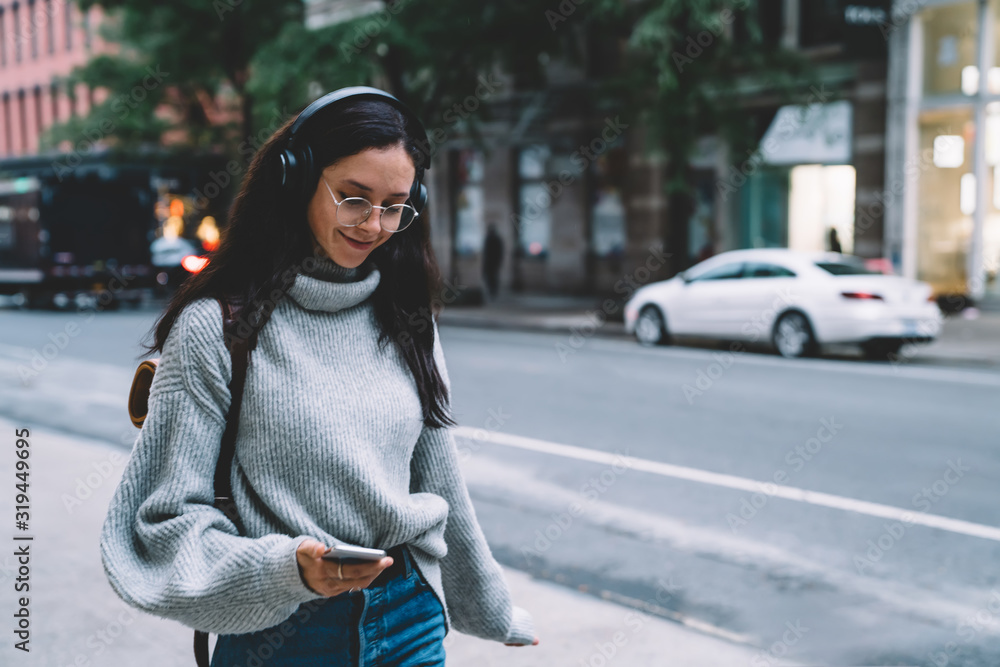 Fototapeta premium Young cheerful woman walking down street and listening to music