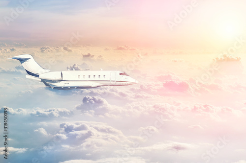 Mid size modern vip private jet flying high in sky over evening fluffy curly clouds at warm colorful sunset time. Luxury small corporate business aircraft trip . Travel beautiful skyline background