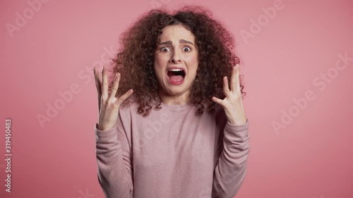Close up of young scared curly girl shouting isolated over pink background. Stressed and depressed woman 4k photo