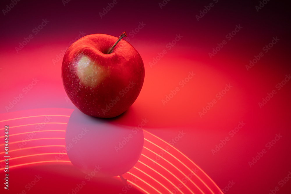 Czerwone jabło na czerwonym malowanym światłem tle - obrazy, fototapety, plakaty 