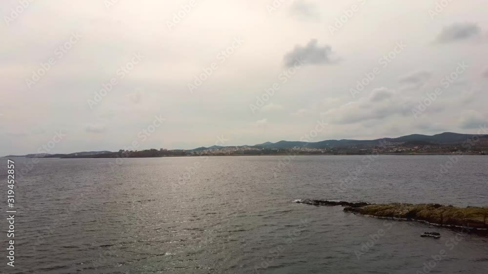 Aerial view of sea in winter with clouds in the sky, coastline with small town and back mountains, Lavrio Greece, moving forward by drone Aerial view of sea in winter with clouds in the sky, coastline with small town and back mountains, Lavrio Greece, moving forward by drone