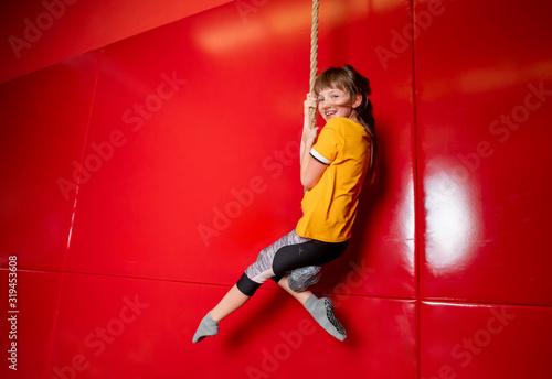 Happy child girl swinging on rope in indoor playground center