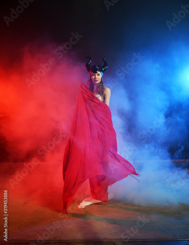 beautiful girl in the clothes of the goddess of the earth with a red veil on a background of smoke