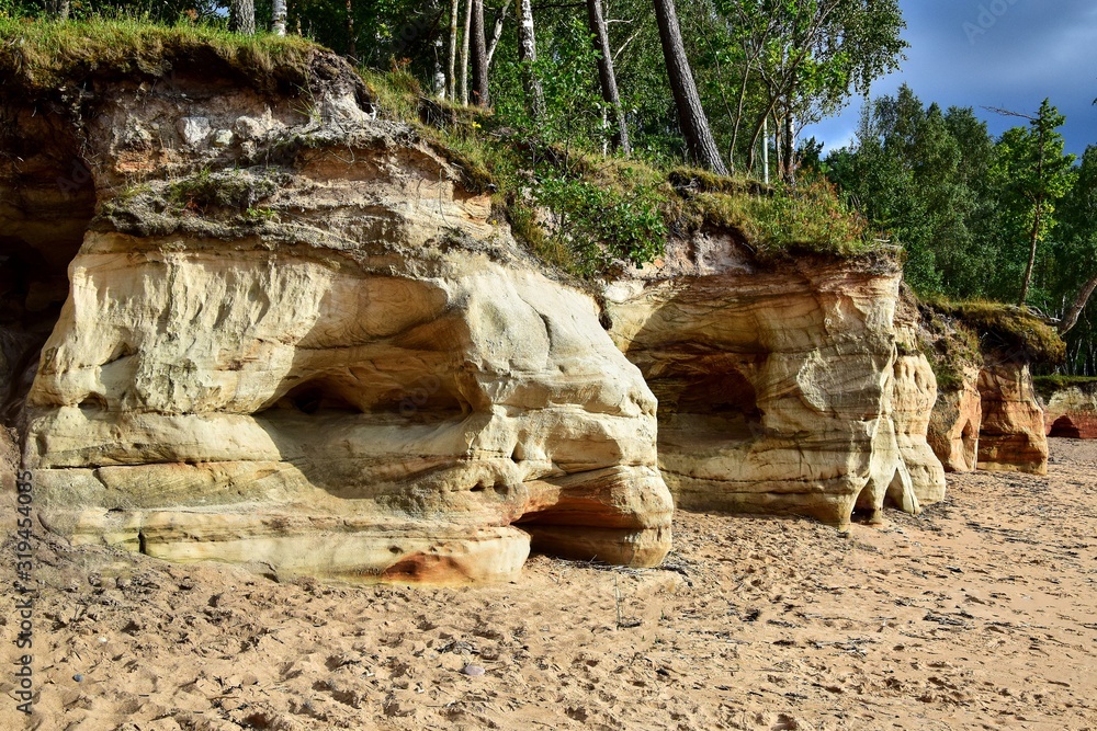 Veczemju klintis, a group of sand cliffs on the Vidzeme coast, red, orange and yellow formations, a sandy beach on the seashore, trees on a hilltop, a beach in Latvia on the shore of the Gulf of Riga. Veczemju klintis, a group of sand cliffs on the Vidzeme coast, red, orange and yellow formations, a sandy beach on the seashore, trees on a hilltop, a beach in Latvia on the shore of the Gulf of Riga.