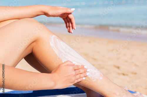 Pretty woman is applying sun cream on her leg with her hand relaxing on the sunbed by the sea