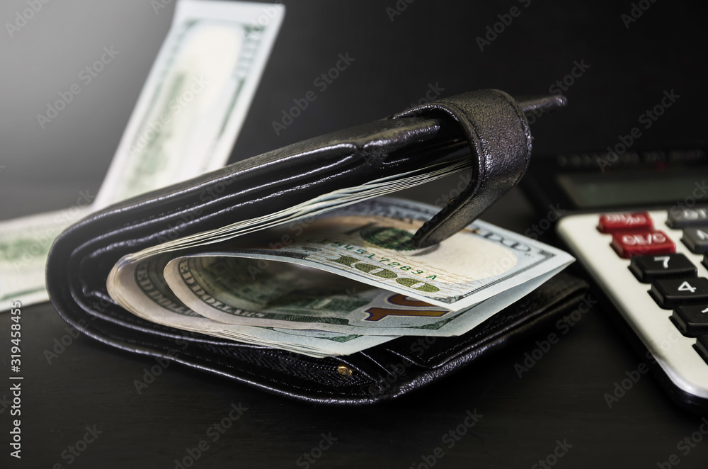 dollars in a black men's wallet and a calculator on a black background. Close-up. Business concept. dollars in a black men's wallet and a calculator on a black background. Close-up. Business concept.