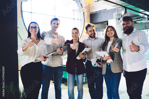 Cheerful colleagues standing together with thumbs up in company