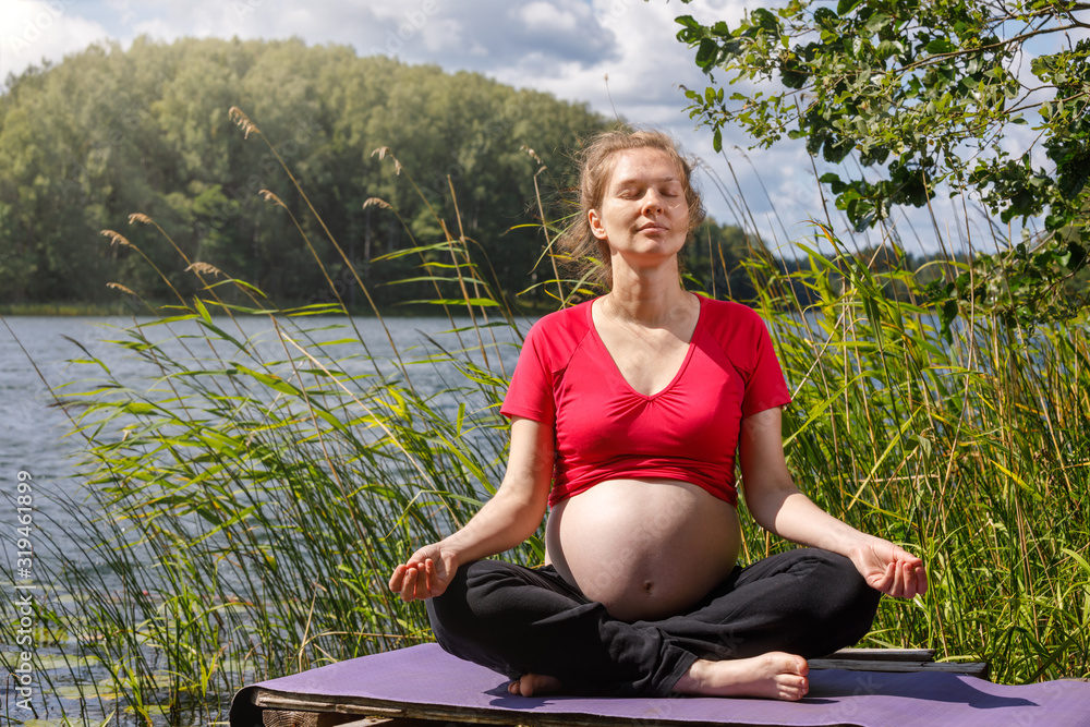 Pregnant woman doing yoga exercise meditating in a summer forest