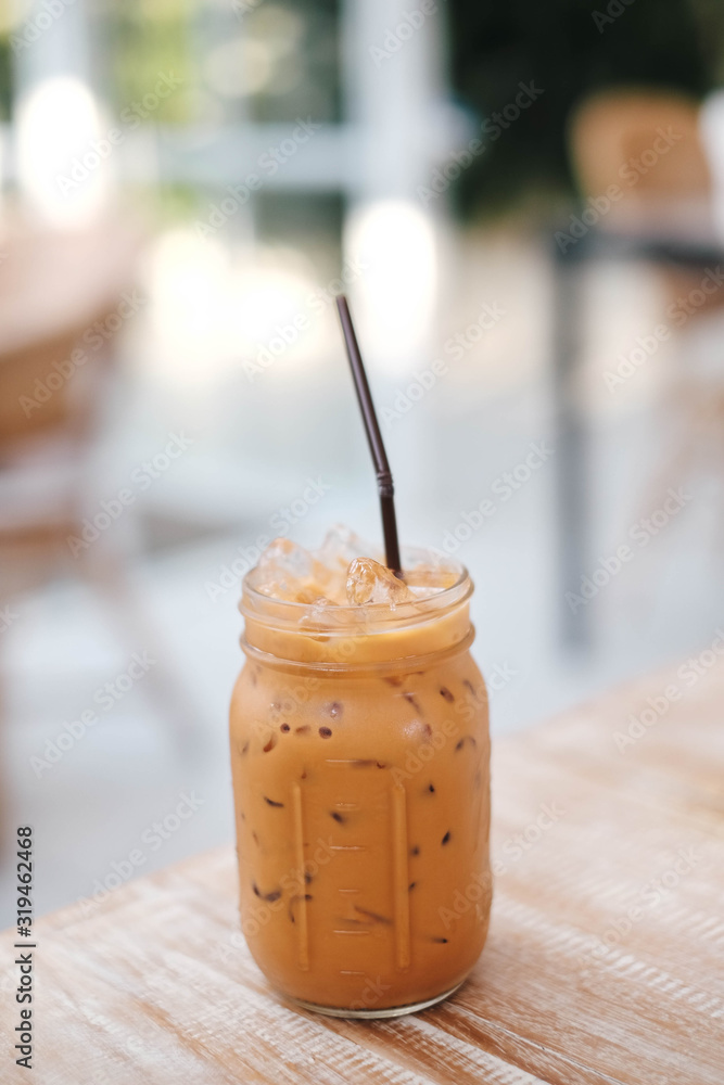 Iced Thai Milk Tea in glass with straw on wooden table in cafe. Iced Thai Milk Tea in glass with straw on wooden table in cafe.