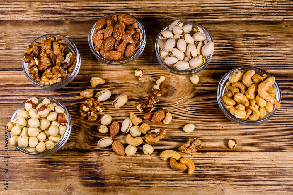 Various nuts (almond, cashew, hazelnut, pistachio, walnut) in glass bowls on a wooden table. Vegetarian meal. Healthy eating concept