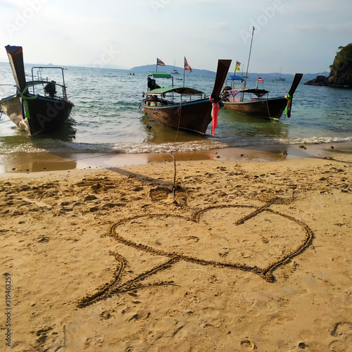 Valentine's day on a sunny beach. Heart drawn in the sand. Traditional Thai wooden long-tailed boats