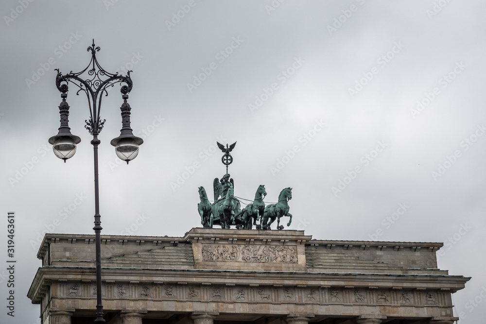 During a cloudy summer day view of Brandenburg gate and an antique street lamp in the foreground, Berlin, Germany.