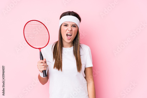 Young caucasian woman playing badminton isolated screaming very angry and aggressive. © Asier