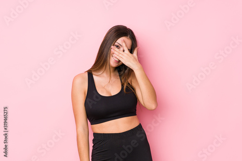 Young fitness caucasian woman isolated blink at the camera through fingers  embarrassed covering face.