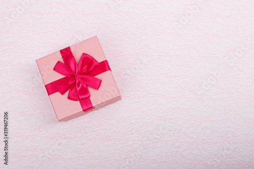 Gift in a pink box on a light pink background with a copy space. Gift box with a red ribbon top view. Simple gift box and copy space