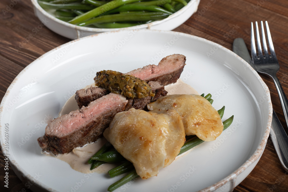 Grilled meat steak New York Striploin. Dumplings with porcini mushrooms in asparagus truffle sauce. On a wooden board on a dark background. Grilled meat steak New York Striploin. Dumplings with porcini mushrooms in asparagus truffle sauce. On a wooden board on a dark background.