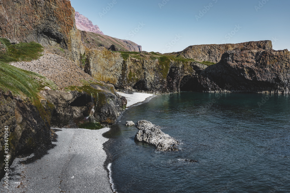 Arctic Beach with small waterfall in Greenland. Near small village of Qeqertarsuaq, Disko Island in Greenland. Blue sky with ocean and green plants.